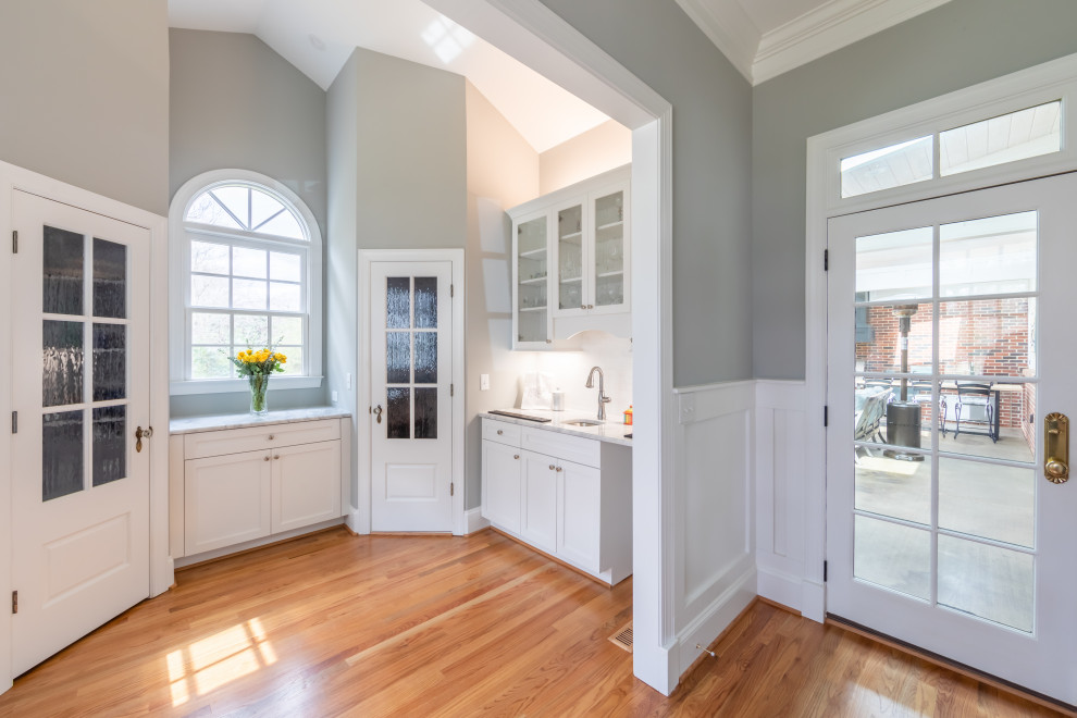 Inspiration for a mid-sized transitional u-shaped medium tone wood floor and brown floor wet bar remodel in Charlotte with an undermount sink, recessed-panel cabinets, white cabinets, quartzite countertops, white backsplash and white countertops