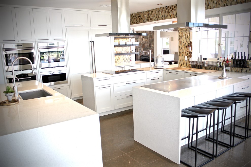 This is an example of a large contemporary l-shaped eat-in kitchen in New York with an undermount sink, shaker cabinets, white cabinets, quartz benchtops, panelled appliances, porcelain floors and multiple islands.