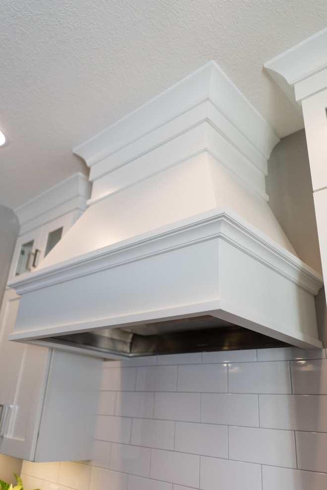 Example of a large transitional u-shaped eat-in kitchen design with a farmhouse sink, flat-panel cabinets, white cabinets, granite countertops, white backsplash, ceramic backsplash, stainless steel appliances and an island