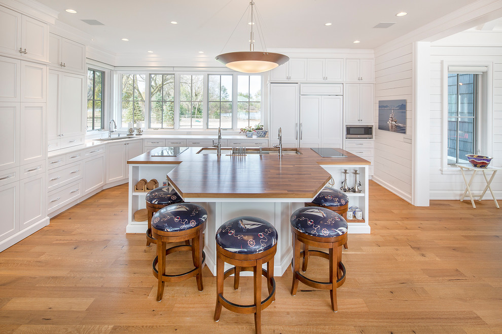 This is an example of a beach style l-shaped kitchen in Omaha with a triple-bowl sink, shaker cabinets, white cabinets, wood benchtops, window splashback, panelled appliances, medium hardwood floors and with island.