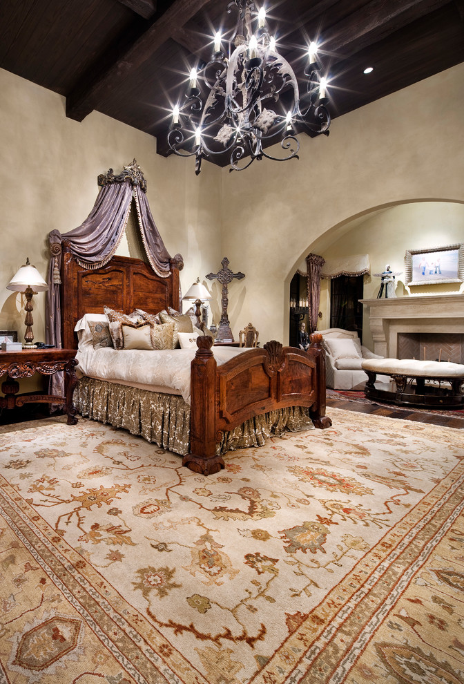 Large mediterranean master bedroom in Austin with beige walls, a standard fireplace and dark hardwood floors.