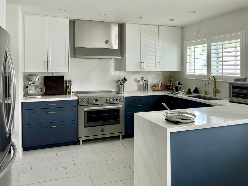 Klassisk inredning av ett vit vitt kök, med skåp i shakerstil, blå skåp, bänkskiva i kvarts, vitt stänkskydd och rostfria vitvaror