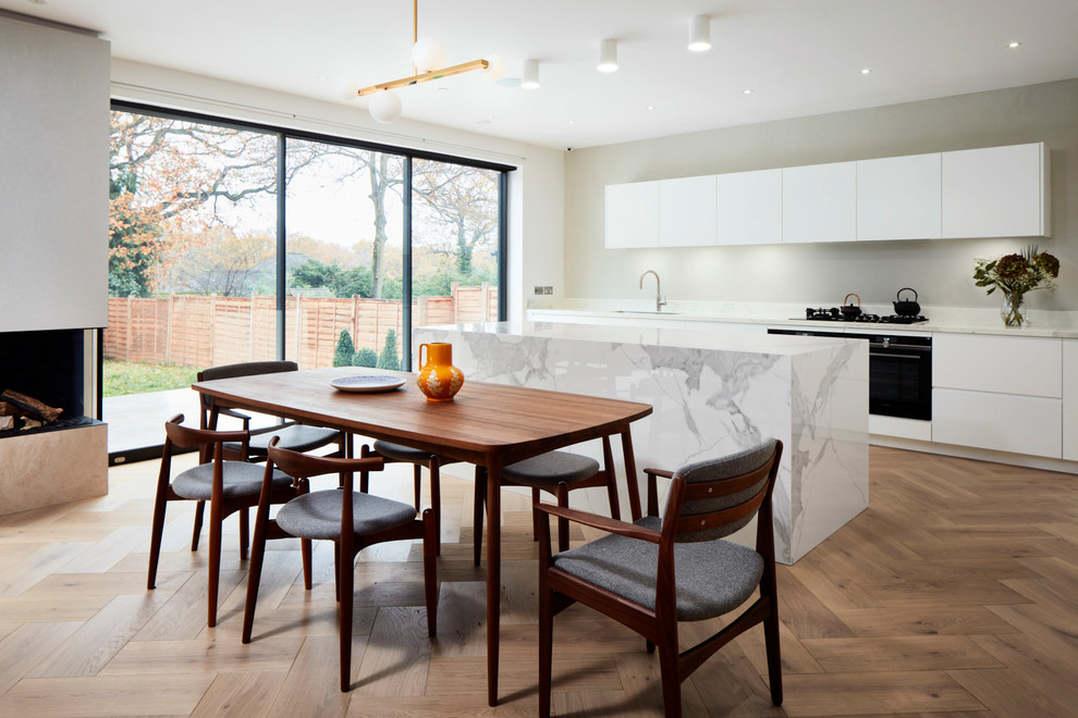 This is an example of a mid-sized contemporary l-shaped open plan kitchen in London with an undermount sink, white cabinets, marble benchtops, white splashback, marble splashback, panelled appliances, with island, white benchtop and flat-panel cabinets.