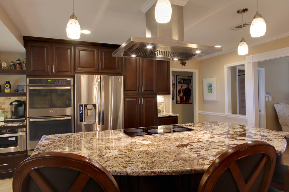 Large transitional l-shaped porcelain tile eat-in kitchen photo in Miami with an undermount sink, raised-panel cabinets, dark wood cabinets, granite countertops, beige backsplash, stone tile backsplash, stainless steel appliances and an island