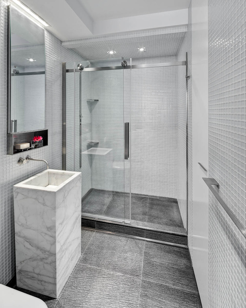 Design ideas for a mid-sized modern 3/4 bathroom in New York with flat-panel cabinets, an alcove shower, a one-piece toilet, gray tile, glass tile, white walls, an integrated sink, marble benchtops, grey floor, a sliding shower screen and grey benchtops.