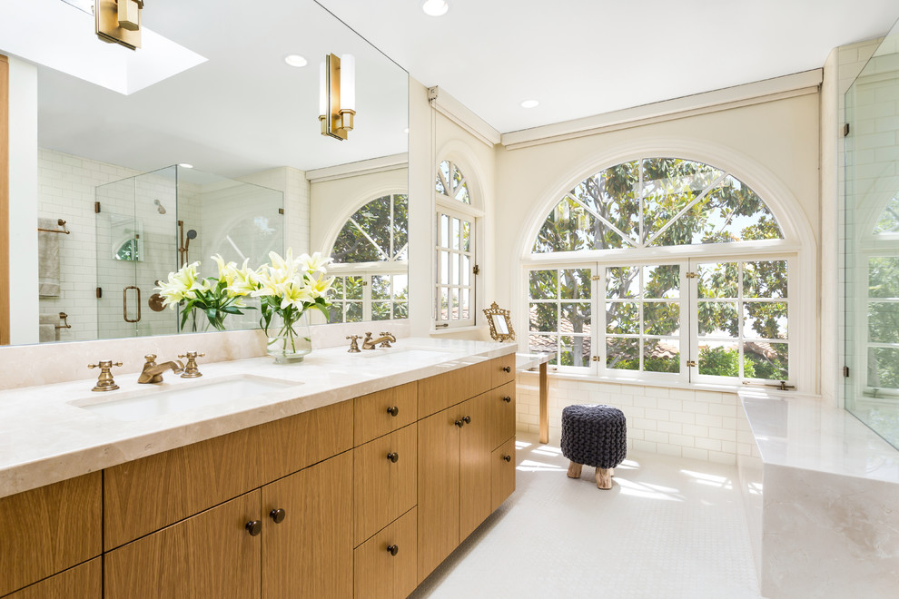 Photo of a large transitional master bathroom in Los Angeles with an undermount sink, flat-panel cabinets, medium wood cabinets, an alcove shower, white tile, subway tile, beige walls, mosaic tile floors, a two-piece toilet, marble benchtops, white floor and a hinged shower door.
