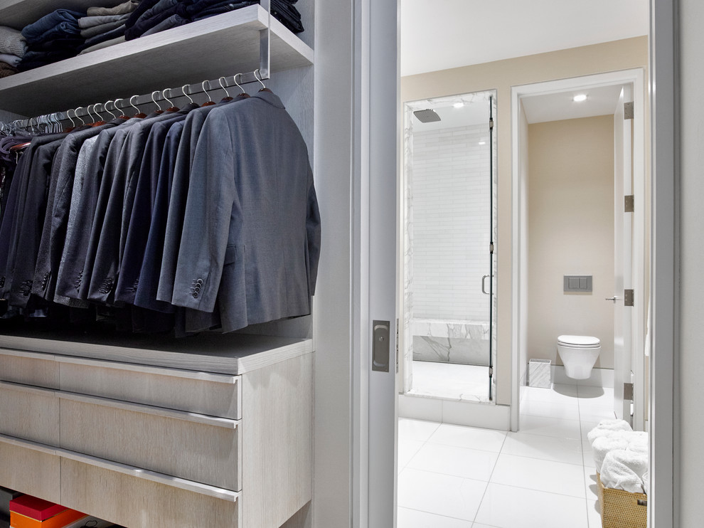 Photo of a mid-sized contemporary men's walk-in wardrobe in New York with flat-panel cabinets, light hardwood floors and grey cabinets.