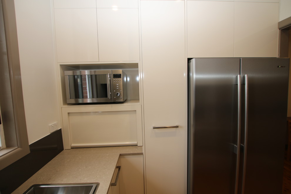 Design ideas for a small contemporary u-shaped kitchen pantry in Sydney with a double-bowl sink, flat-panel cabinets, beige cabinets, quartz benchtops, metallic splashback, glass sheet splashback, stainless steel appliances, light hardwood floors and no island.