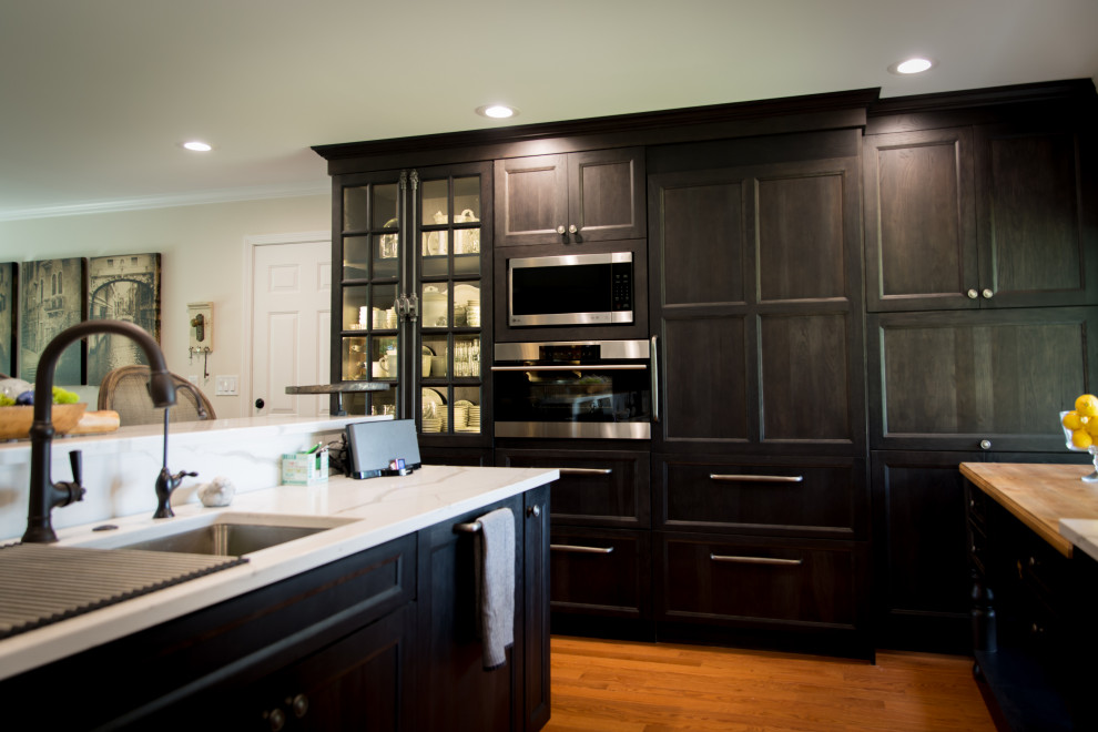 Large mountain style l-shaped light wood floor and brown floor eat-in kitchen photo with an undermount sink, recessed-panel cabinets, dark wood cabinets, quartz countertops, white backsplash, stainless steel appliances, an island, white countertops and quartz backsplash