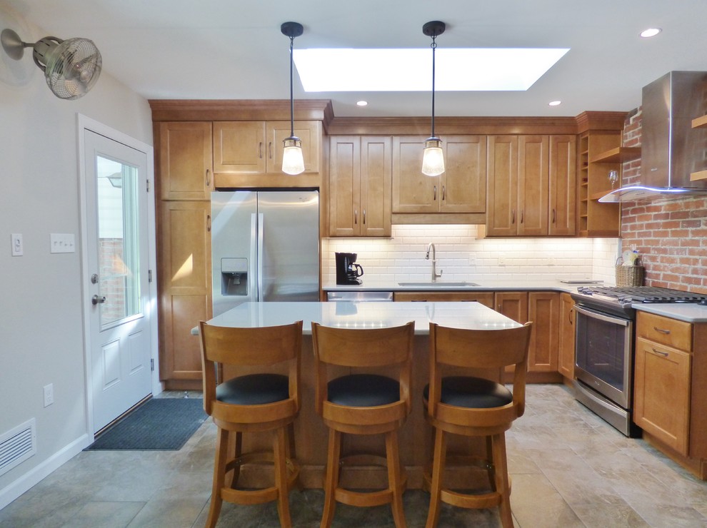 Inspiration for a transitional l-shaped porcelain tile eat-in kitchen remodel with an undermount sink, recessed-panel cabinets, medium tone wood cabinets, quartz countertops, white backsplash, subway tile backsplash, stainless steel appliances and an island