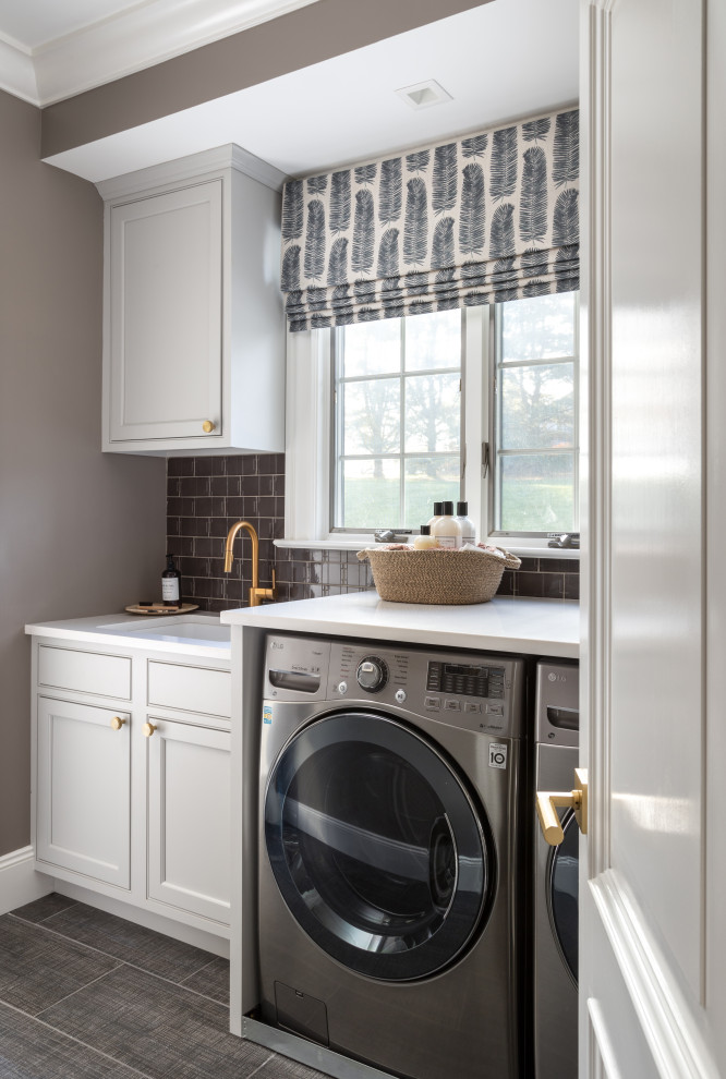 Mid-sized transitional galley ceramic tile and brown floor dedicated laundry room photo in Baltimore with a drop-in sink, recessed-panel cabinets, gray cabinets, quartz countertops, brown backsplash, ceramic backsplash, brown walls, a side-by-side washer/dryer and white countertops