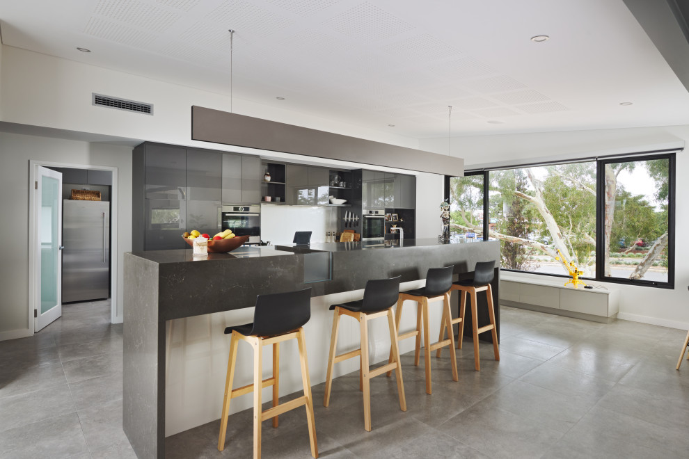 Photo of an expansive modern galley kitchen pantry in Perth with an undermount sink, beaded inset cabinets, grey cabinets, granite benchtops, white splashback, glass sheet splashback, stainless steel appliances, porcelain floors, with island, grey floor, grey benchtop and vaulted.