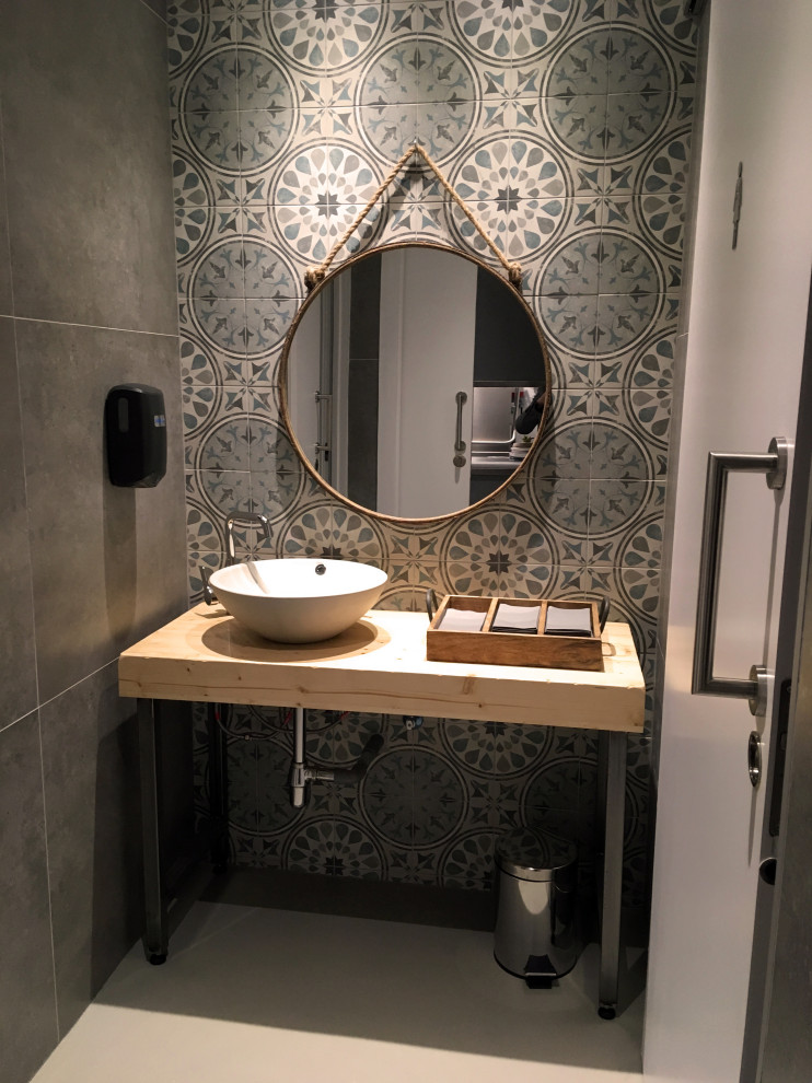 Design ideas for a mid-sized industrial powder room in Barcelona with grey walls, concrete floors, grey floor, open cabinets, grey cabinets, a two-piece toilet, green tile, cement tile, a vessel sink, wood benchtops and beige benchtops.