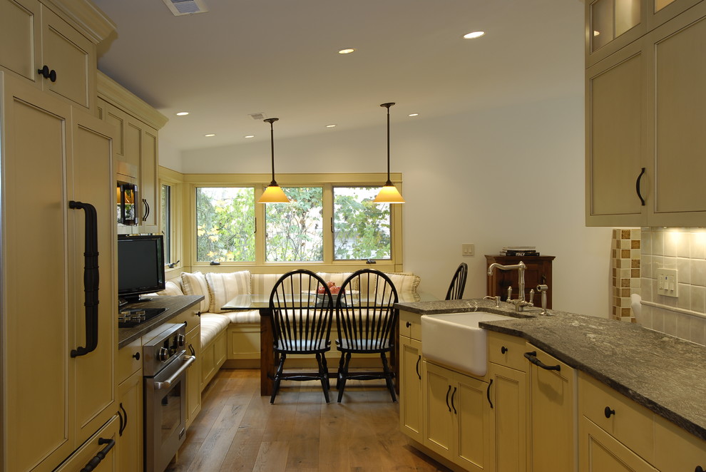 Inspiration for a small transitional galley eat-in kitchen in New York with a farmhouse sink, recessed-panel cabinets, yellow cabinets, granite benchtops, beige splashback, porcelain splashback, stainless steel appliances and light hardwood floors.