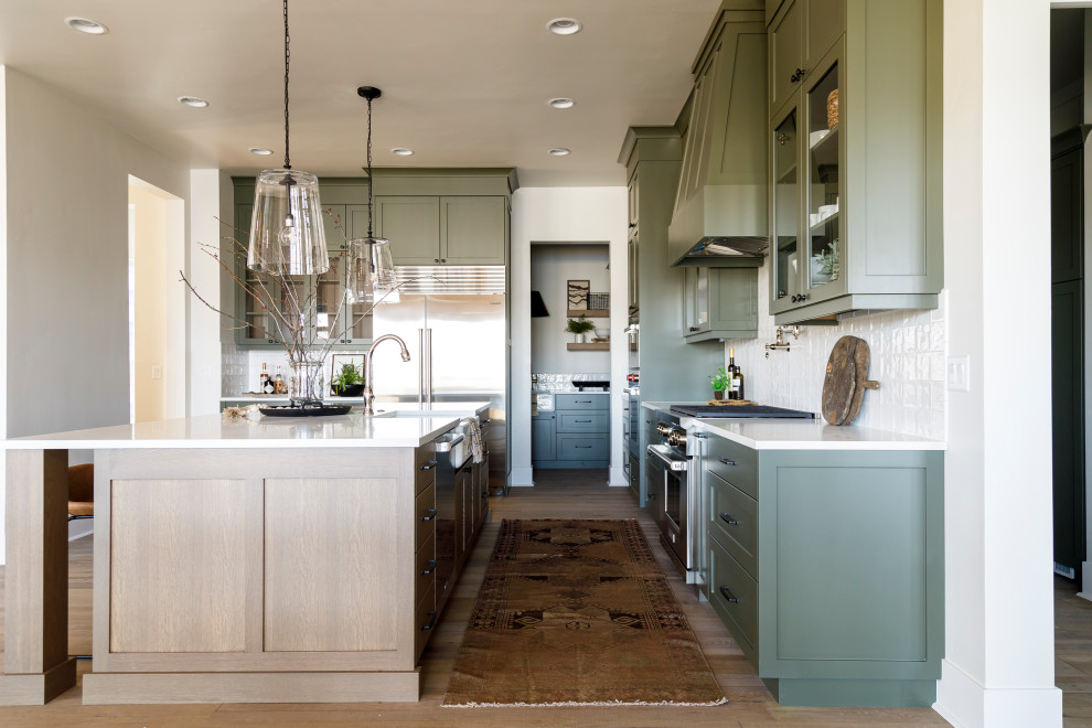 Inspiration for a mid-sized farmhouse l-shaped medium tone wood floor eat-in kitchen remodel in Boise with a farmhouse sink, shaker cabinets, green cabinets, quartz countertops, white backsplash, ceramic backsplash, stainless steel appliances, an island and white countertops