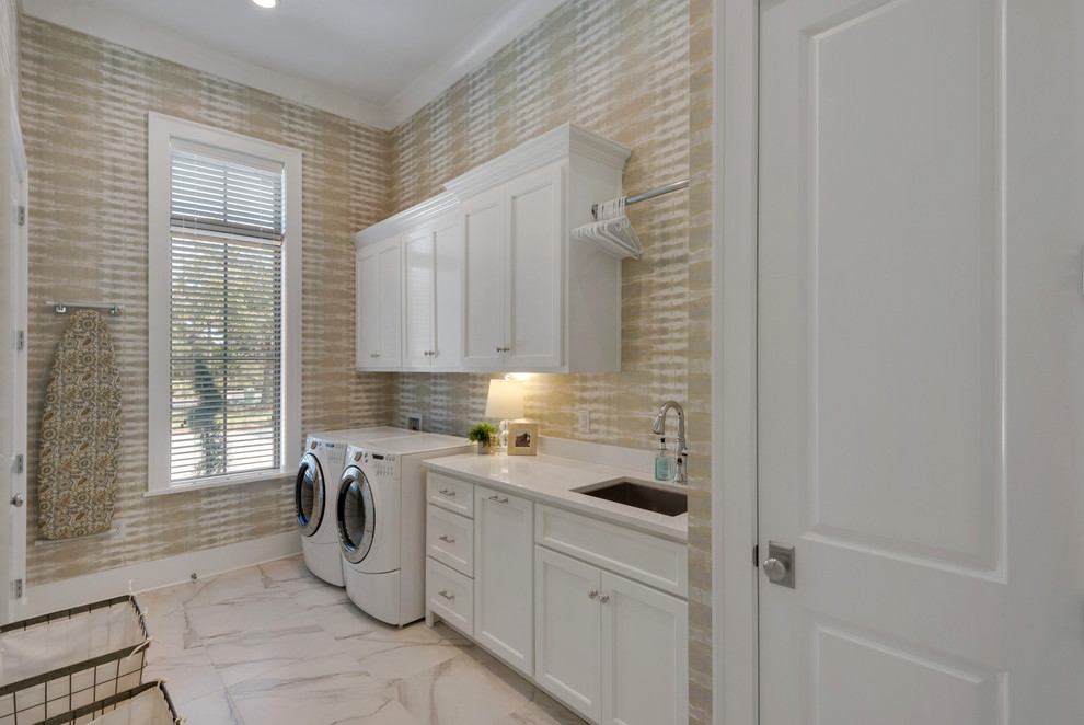 Photo of a large beach style galley utility room in Other with an undermount sink, shaker cabinets, white cabinets, beige walls and a side-by-side washer and dryer.