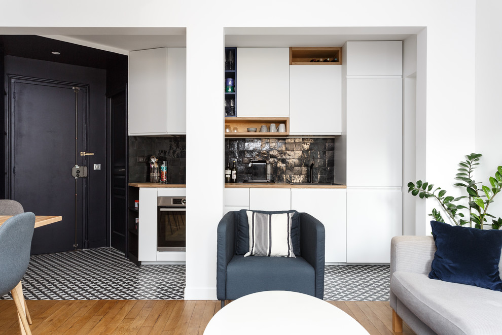 Design ideas for a small contemporary single-wall open plan kitchen in Paris with a single-bowl sink, flat-panel cabinets, white cabinets, wood benchtops, black splashback, terra-cotta splashback, stainless steel appliances, cement tiles, no island, black floor and beige benchtop.