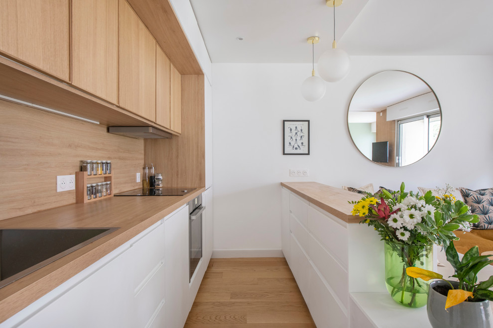 Photo of a small contemporary galley eat-in kitchen in Paris with a drop-in sink, flat-panel cabinets, white cabinets, wood benchtops, beige splashback, timber splashback, panelled appliances, light hardwood floors, a peninsula, beige floor and beige benchtop.