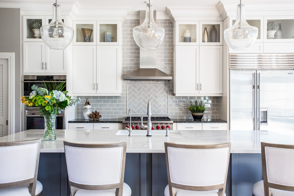 Inspiration for a transitional galley kitchen in Dallas with an undermount sink, shaker cabinets, white cabinets, grey splashback, subway tile splashback, stainless steel appliances, with island and white benchtop.