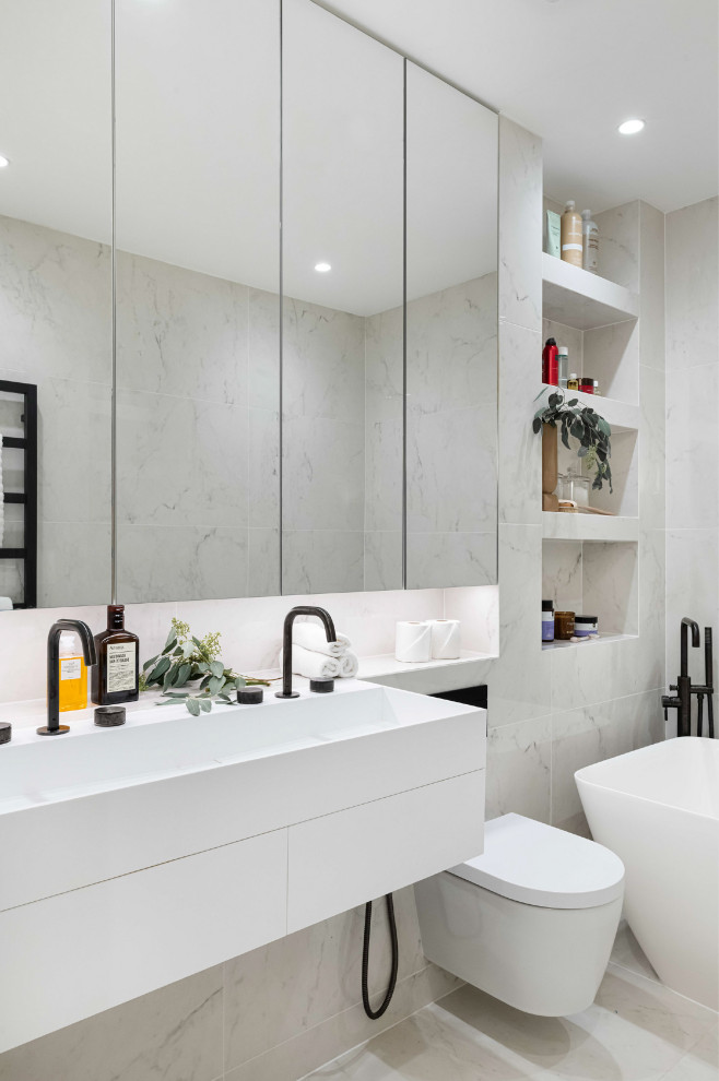 Photo of a large contemporary ensuite bathroom in London with flat-panel cabinets, white cabinets, a wall mounted toilet, white tiles, ceramic tiles, ceramic flooring, white floors, a wall niche, double sinks, a floating vanity unit and a console sink.