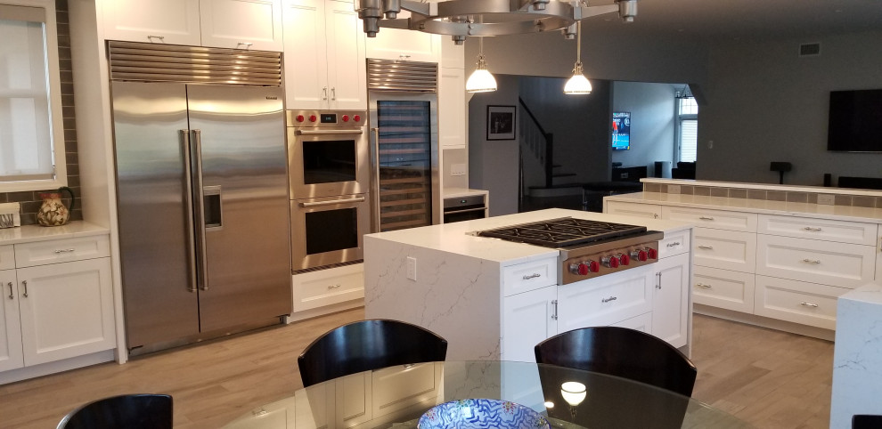 Classic u-shaped kitchen/diner in New York with a belfast sink, recessed-panel cabinets, white cabinets, engineered stone countertops, grey splashback, glass tiled splashback, stainless steel appliances, porcelain flooring, an island, brown floors and multicoloured worktops.