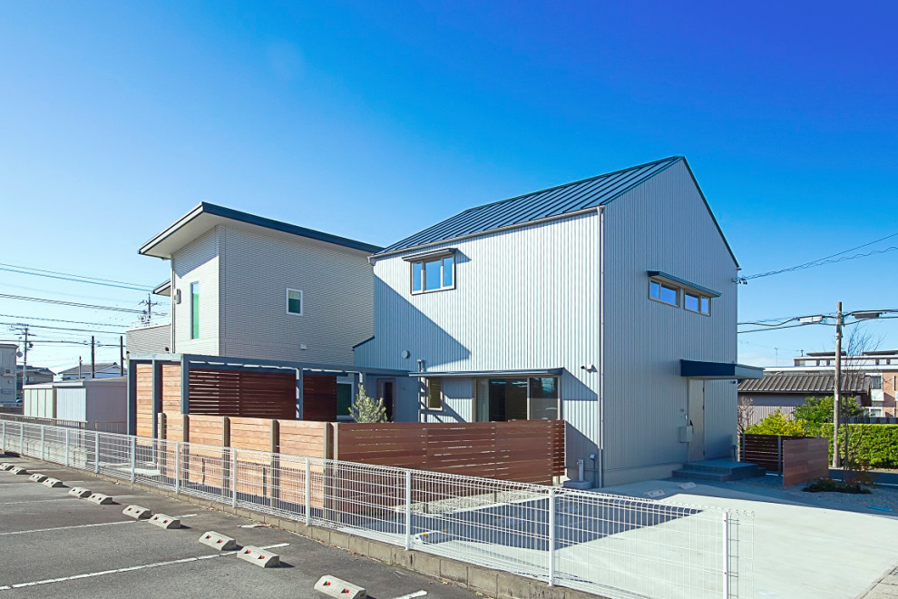 Cette photo montre une façade de maison métallique et grise scandinave en planches et couvre-joints à un étage avec un toit à deux pans, un toit en métal et un toit bleu.