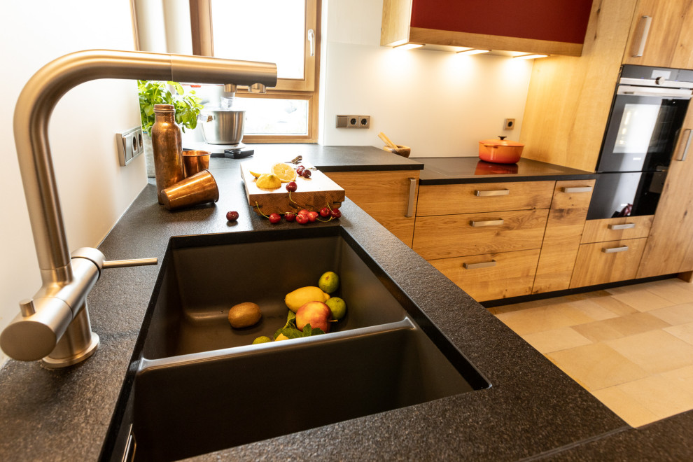 Photo of a large contemporary u-shaped open plan kitchen in Nuremberg with a submerged sink, flat-panel cabinets, medium wood cabinets, granite worktops, white splashback, glass sheet splashback, black appliances, terracotta flooring, a breakfast bar, black worktops and exposed beams.
