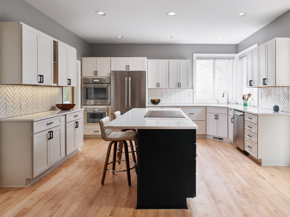 Inspiration for a large contemporary u-shaped open plan kitchen in Portland with an undermount sink, shaker cabinets, white cabinets, quartz benchtops, white splashback, ceramic splashback, stainless steel appliances, light hardwood floors, with island, multi-coloured floor and white benchtop.