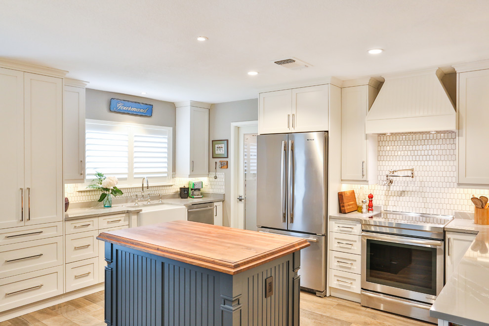 Mid-sized country u-shaped eat-in kitchen in Austin with a farmhouse sink, shaker cabinets, white cabinets, quartz benchtops, porcelain splashback, stainless steel appliances, porcelain floors, with island, grey benchtop, white splashback and brown floor.