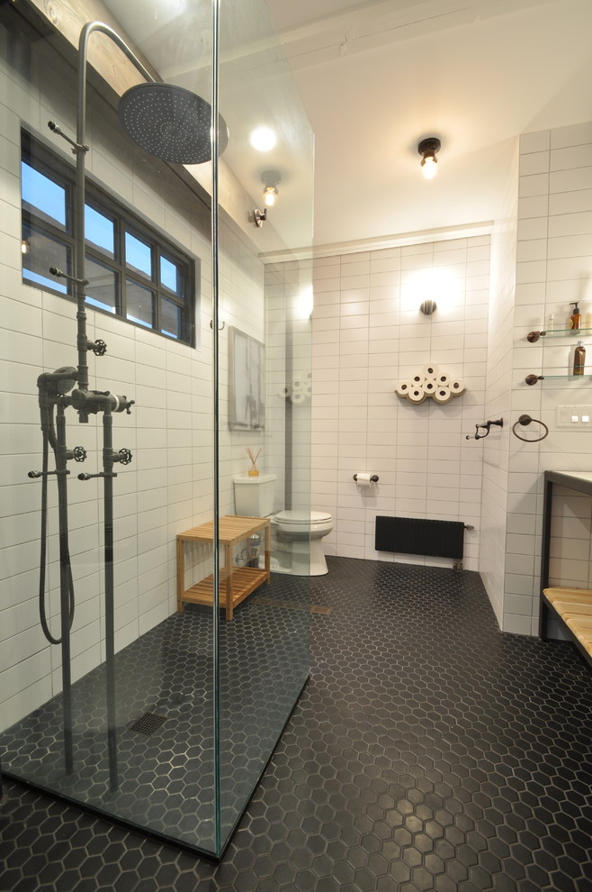 Inspiration for a mid-sized industrial master bathroom in New York with open cabinets, light wood cabinets, an open shower, a one-piece toilet, white tile, white walls, ceramic floors, granite benchtops, an integrated sink, subway tile, black floor and an open shower.