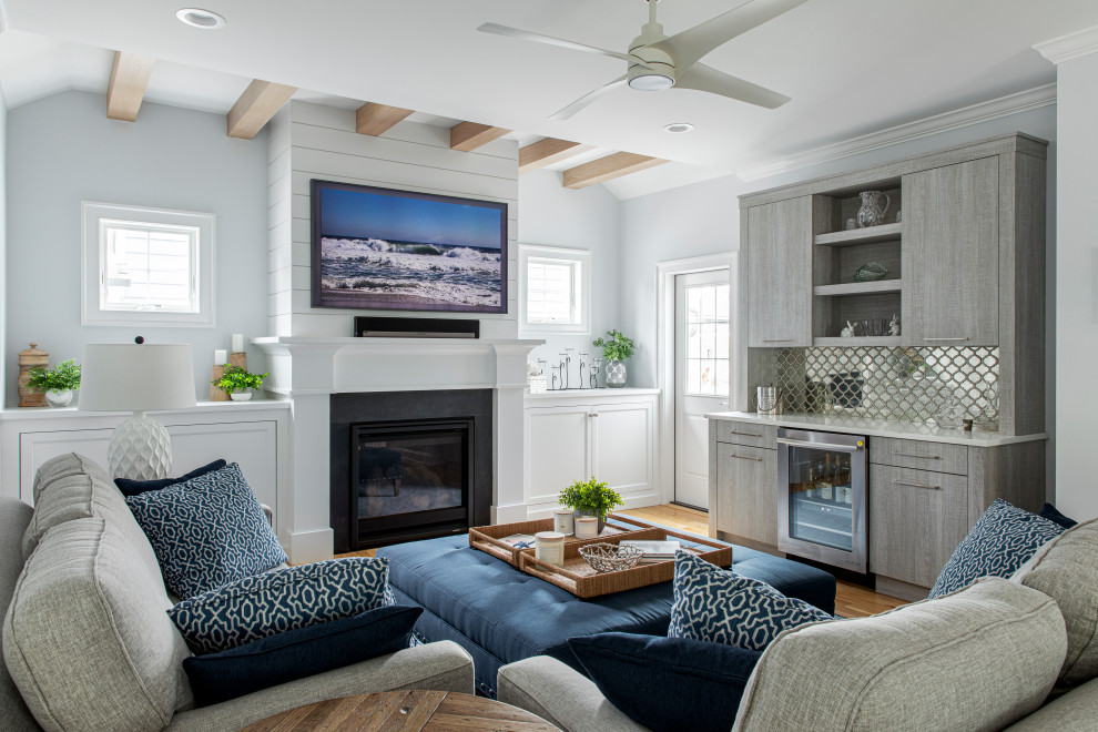 This is an example of a beach style open concept family room in New York with a home bar, grey walls, light hardwood floors, a standard fireplace, a stone fireplace surround and a wall-mounted tv.