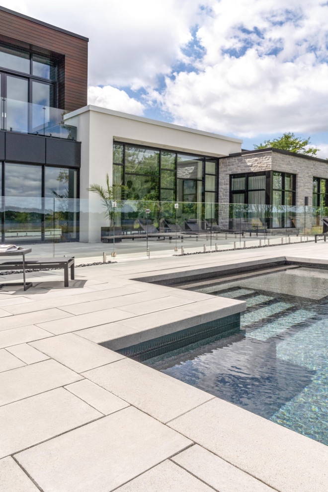 Diseño de piscina alargada minimalista grande rectangular en patio trasero con paisajismo de piscina y losas de hormigón