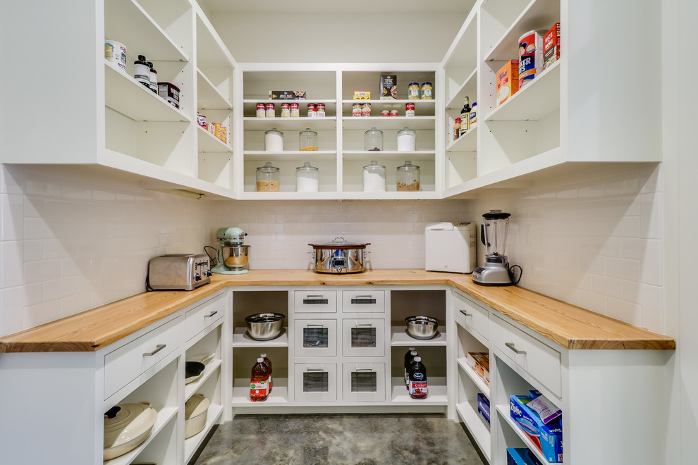 Large country u-shaped kitchen pantry in Jackson with a farmhouse sink, open cabinets, white cabinets, wood benchtops, white splashback, subway tile splashback, stainless steel appliances, concrete floors, with island and grey floor.