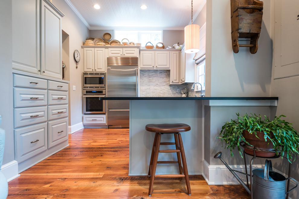 Inspiration for a mid-sized transitional u-shaped brown floor and medium tone wood floor enclosed kitchen remodel in Charleston with an undermount sink, raised-panel cabinets, white cabinets, soapstone countertops, gray backsplash, matchstick tile backsplash, stainless steel appliances and a peninsula