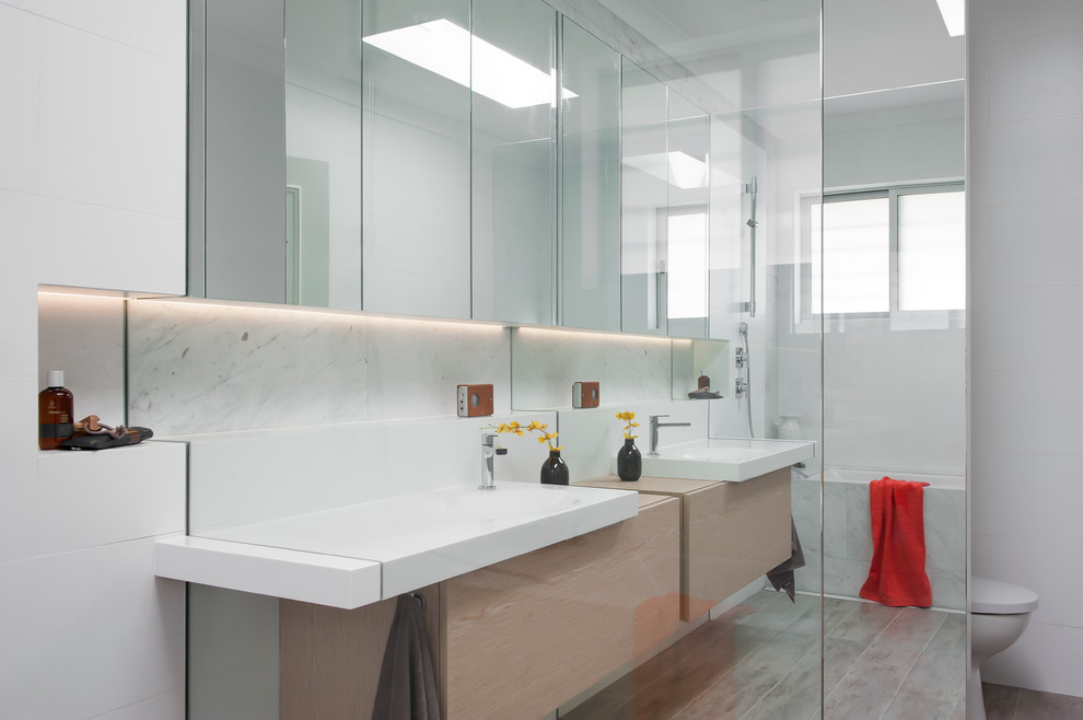 Design ideas for a small contemporary 3/4 bathroom in Sydney with a wall-mount sink, furniture-like cabinets, light wood cabinets, solid surface benchtops, an undermount tub, an open shower, a wall-mount toilet, white tile, ceramic tile, white walls and ceramic floors.