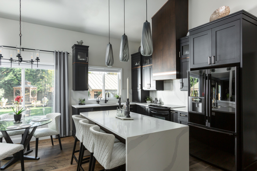 Mid-sized transitional l-shaped medium tone wood floor, brown floor and vaulted ceiling eat-in kitchen photo in Seattle with a single-bowl sink, shaker cabinets, black cabinets, quartz countertops, white backsplash, quartz backsplash, black appliances, an island and white countertops