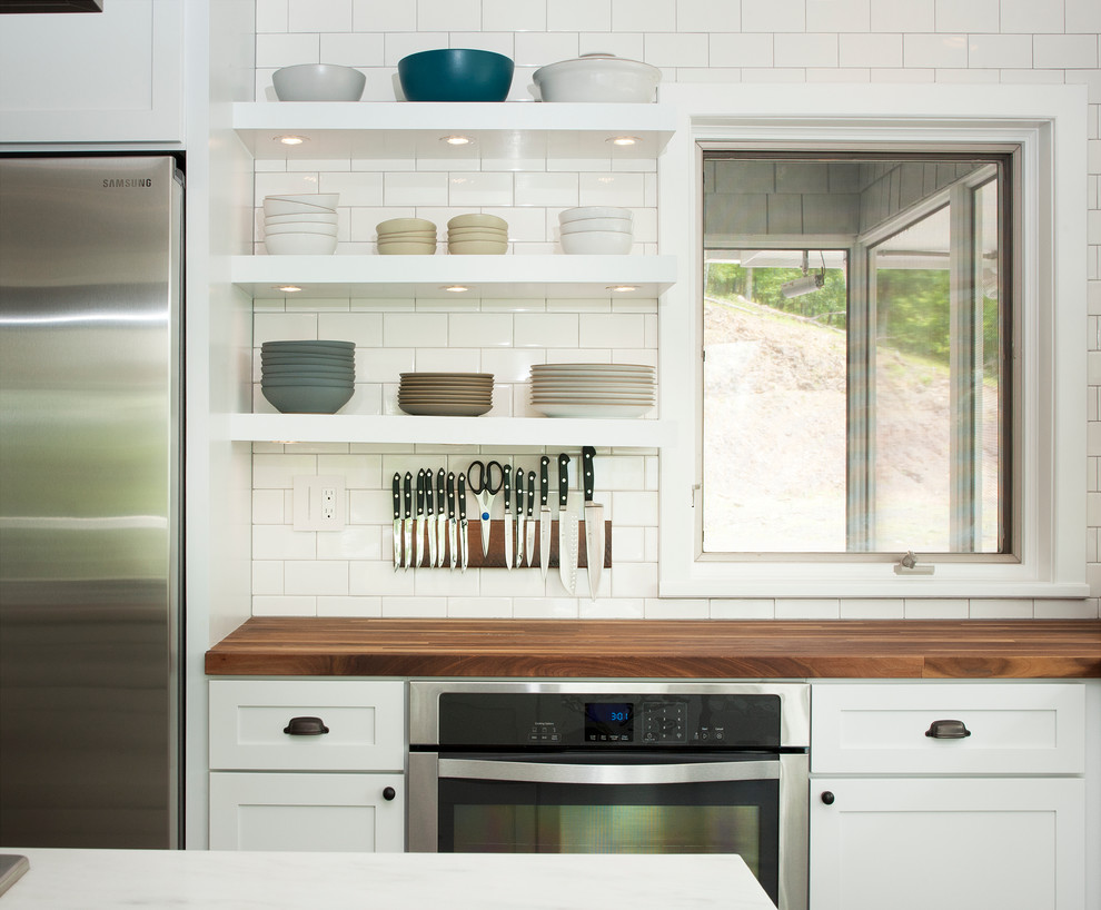 Photo of a transitional kitchen in New York with a farmhouse sink, shaker cabinets, white cabinets, wood benchtops, white splashback, ceramic splashback, stainless steel appliances and medium hardwood floors.