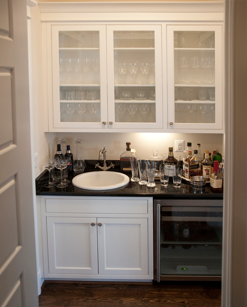 Small traditional single-wall wet bar in DC Metro with a drop-in sink, shaker cabinets, white cabinets, solid surface benchtops and dark hardwood floors.