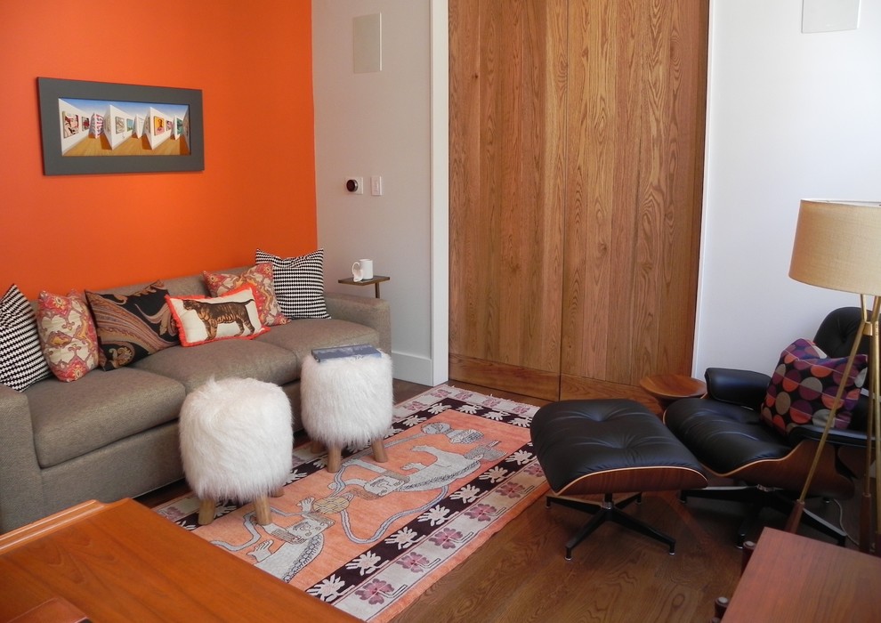 This is an example of a small modern home office in New York with a library, orange walls, medium hardwood floors, no fireplace, a freestanding desk and brown floor.