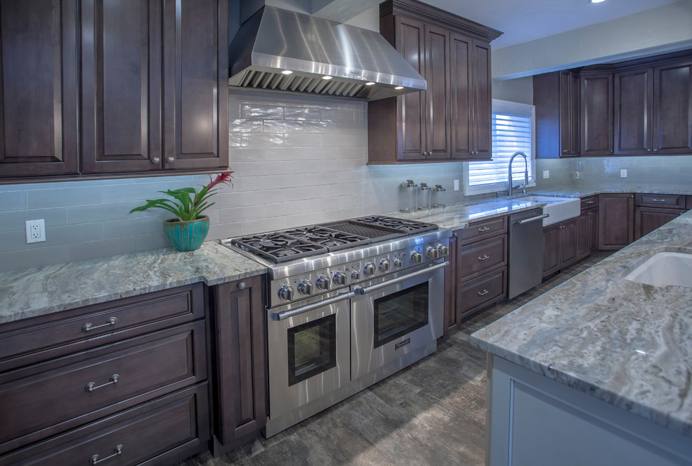 This is an example of a large contemporary l-shaped open plan kitchen in Miami with a farmhouse sink, raised-panel cabinets, dark wood cabinets, granite benchtops, grey splashback, subway tile splashback, stainless steel appliances, dark hardwood floors, multiple islands and brown floor.
