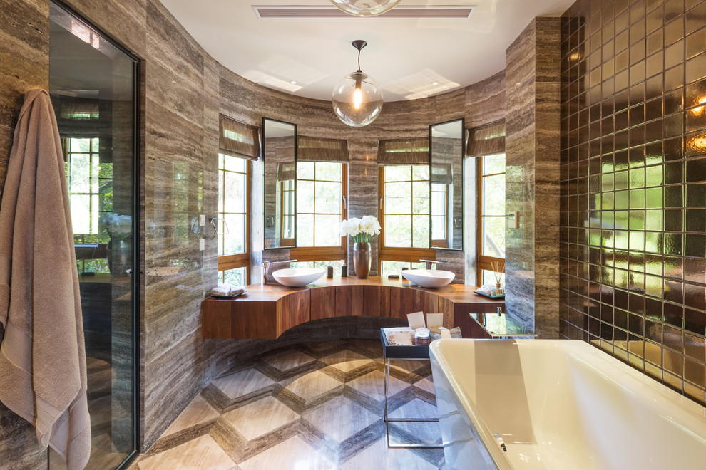 This is an example of a contemporary master bathroom in Miami with medium wood cabinets, a freestanding tub, stone slab, brown walls, a vessel sink, wood benchtops, beige floor and a hinged shower door.