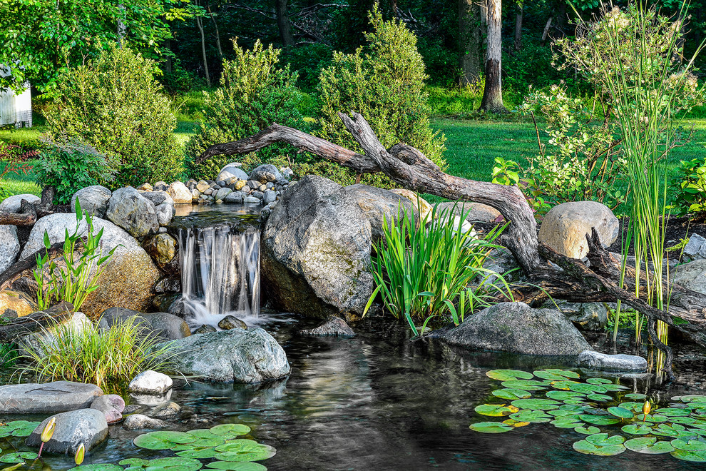 This is an example of a large country backyard garden for spring in New York with a water feature.