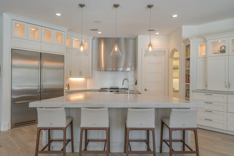 Large transitional u-shaped open plan kitchen in Houston with shaker cabinets, white cabinets, with island, quartzite benchtops, white splashback, glass tile splashback, stainless steel appliances, a double-bowl sink, light hardwood floors and beige floor.