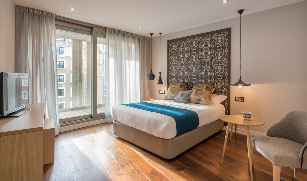 Mid-sized contemporary master bedroom in Madrid with beige walls, medium hardwood floors and no fireplace.