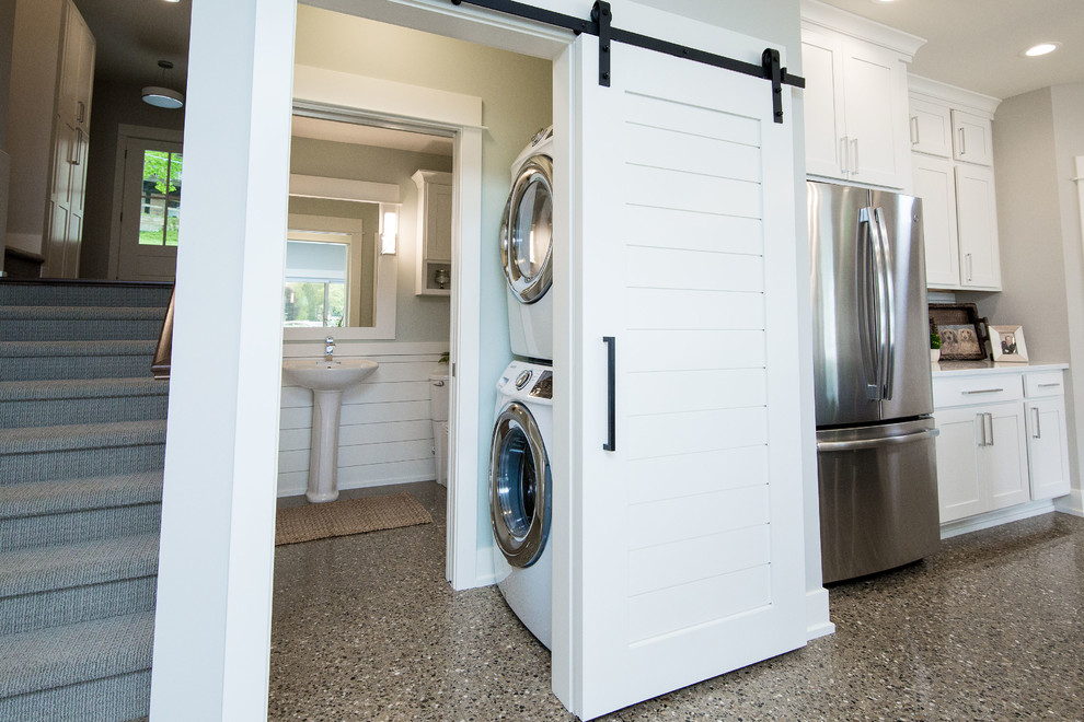 This is an example of a small transitional single-wall dedicated laundry room in Grand Rapids with white splashback, ceramic splashback, concrete floors, grey floor, a stacked washer and dryer and grey walls.