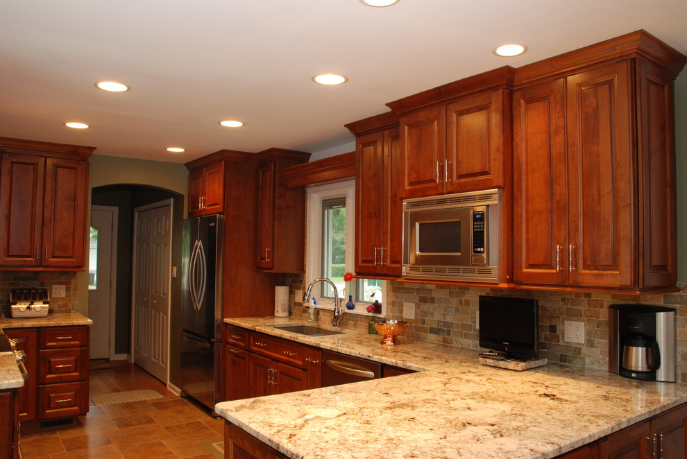 Photo of a mid-sized country l-shaped eat-in kitchen in Chicago with a double-bowl sink, raised-panel cabinets, medium wood cabinets, stainless steel appliances and a peninsula.