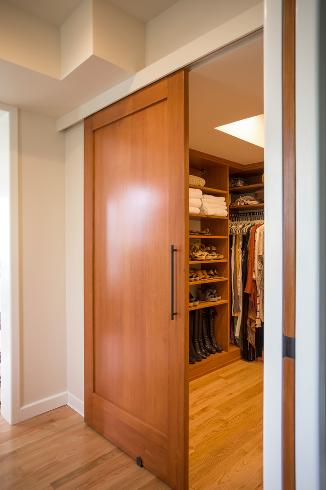 Photo of a large modern gender-neutral dressing room in Seattle with flat-panel cabinets, medium wood cabinets and light hardwood floors.