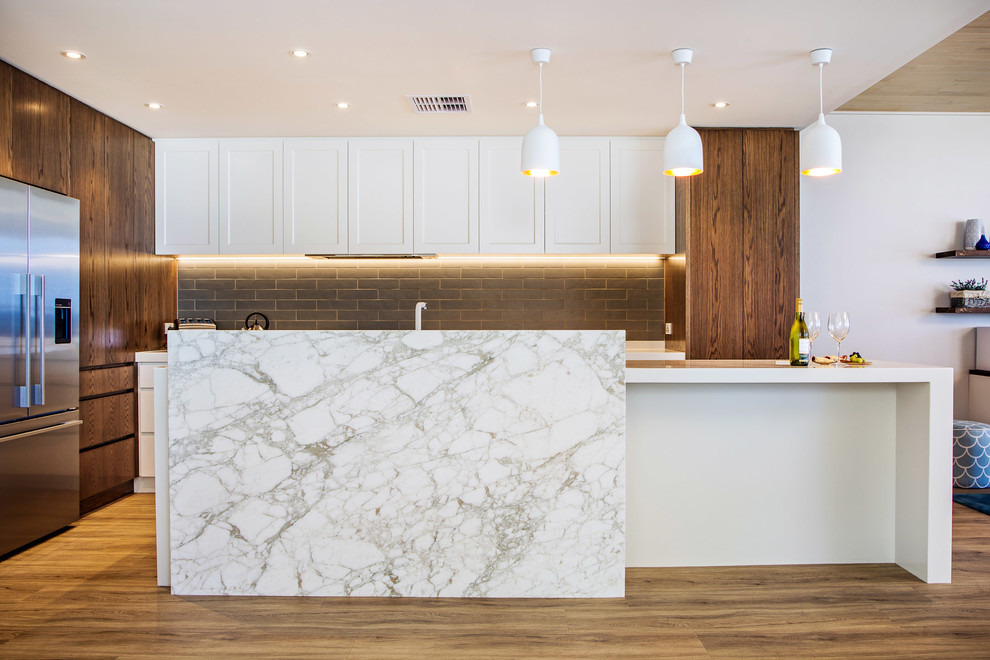 This is an example of a mid-sized beach style galley open plan kitchen in Brisbane with an undermount sink, recessed-panel cabinets, white cabinets, quartz benchtops, grey splashback, subway tile splashback, stainless steel appliances, vinyl floors and with island.
