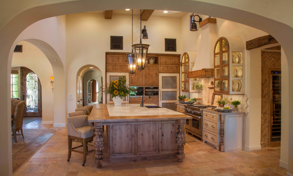 This is an example of a large country l-shaped eat-in kitchen in San Diego with a farmhouse sink, glass-front cabinets, distressed cabinets, marble benchtops, multi-coloured splashback, terra-cotta splashback, terra-cotta floors, with island, beige floor, beige benchtop, exposed beam and stainless steel appliances.