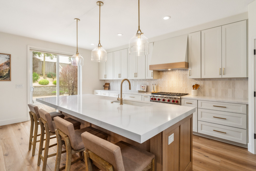 Inspiration for a transitional galley medium tone wood floor and brown floor kitchen remodel with an undermount sink, recessed-panel cabinets, white cabinets, beige backsplash, stainless steel appliances, an island and beige countertops
